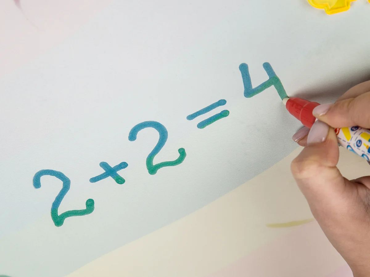 A hand writing 2 + 2 = 4 on the mat with a water marker